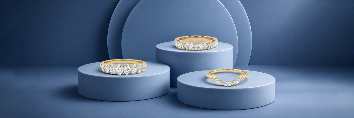 Three lab-grown diamond wedding bands in yellow gold — five-stone round brilliant shared prong band, mixed fancy cut half eternity band with kite and baguette diamonds, and curved marquise chevron band on blue cylinder pedestals