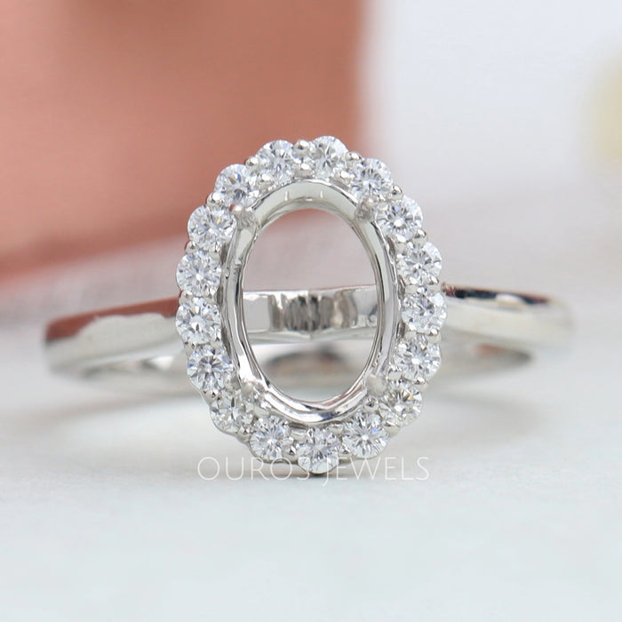 front view of oval-shaped halo semi-mount engagement ring on grey fabric