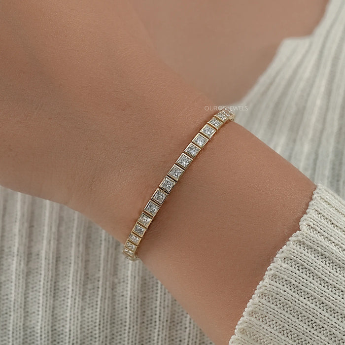 princess cut ethically grown diamonds bezel set tennis bracelet in yellow gold on hand