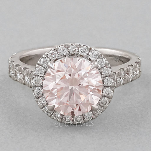 front view of pink round-cut diamond solitaire halo engagement ring on grey fabric