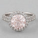 front view of pink round-cut diamond solitaire halo engagement ring on grey fabric