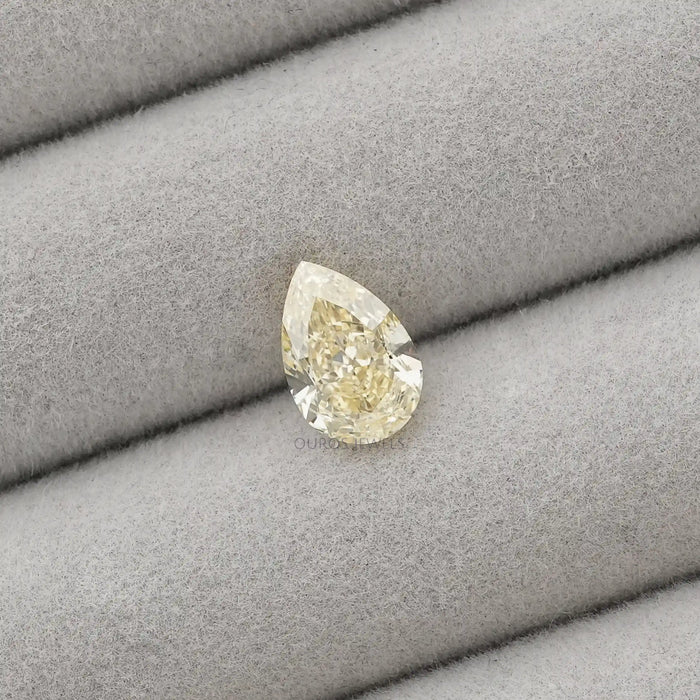 2.17 Carat Fancy Yellow Pear Cut Loose Diamond displayed on a gray cushioned surface, showcasing its elegant shape and yellow color.