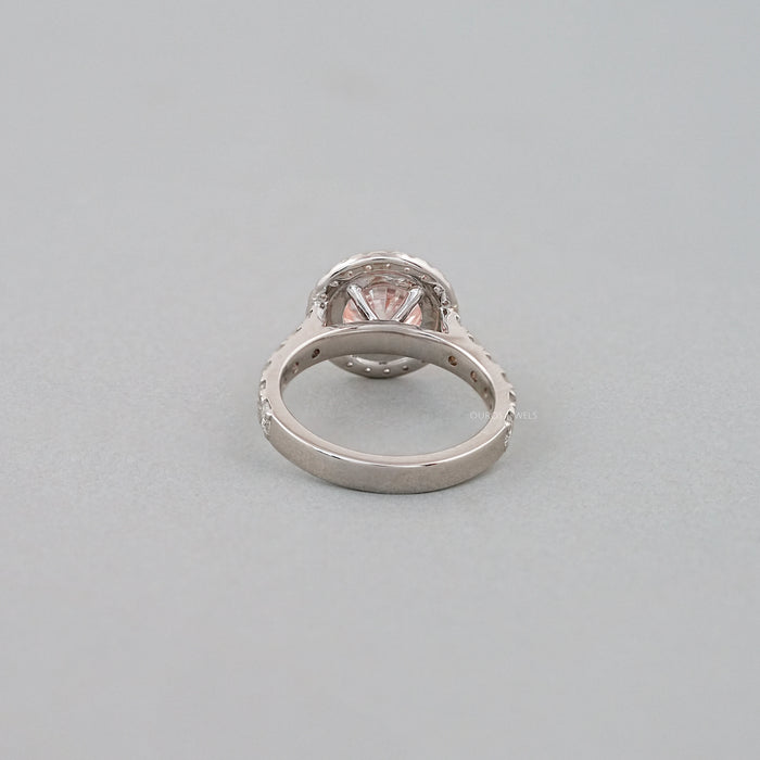 back view of pink round-cut diamond solitaire halo engagement ring on grey fabric