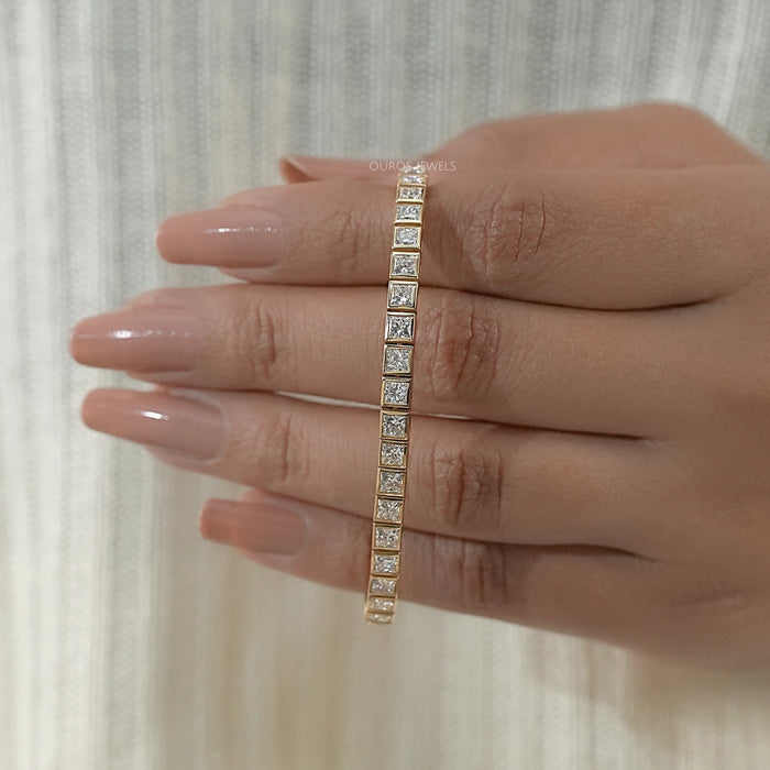 princess cut ethically sourced diamonds bezel set tennis bracelet in yellow gold on hand