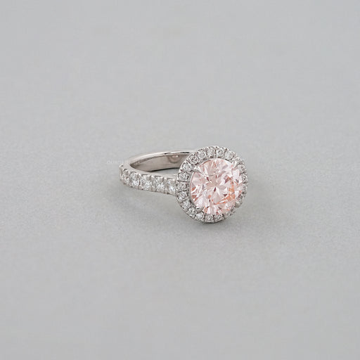 side view of pink round-cut diamond solitaire halo engagement ring on grey fabric