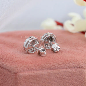 Cluster Round Cut Diamond Stud Earrings showing the back view of the earrings, displayed on a soft pink fabric surface with a delicate background of blurred white and red flowers.