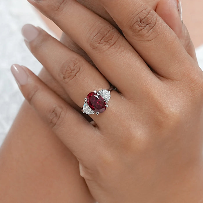 oval ruby gemstone and half moon diamond 3 stone engagement ring on model's finger