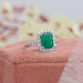 green emerald cut gemstone halo engagement ring's side view on jewelry box