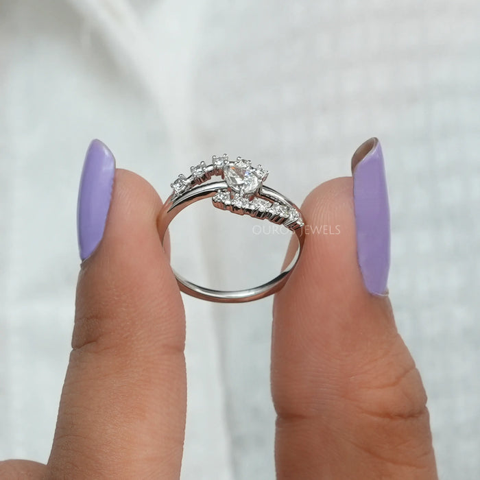 The diamond is cut in a pear shape, giving it a beautiful sparkle that catches the eye. The setting creates a twisted or crossover design, with each end of the band curving away from the center stone