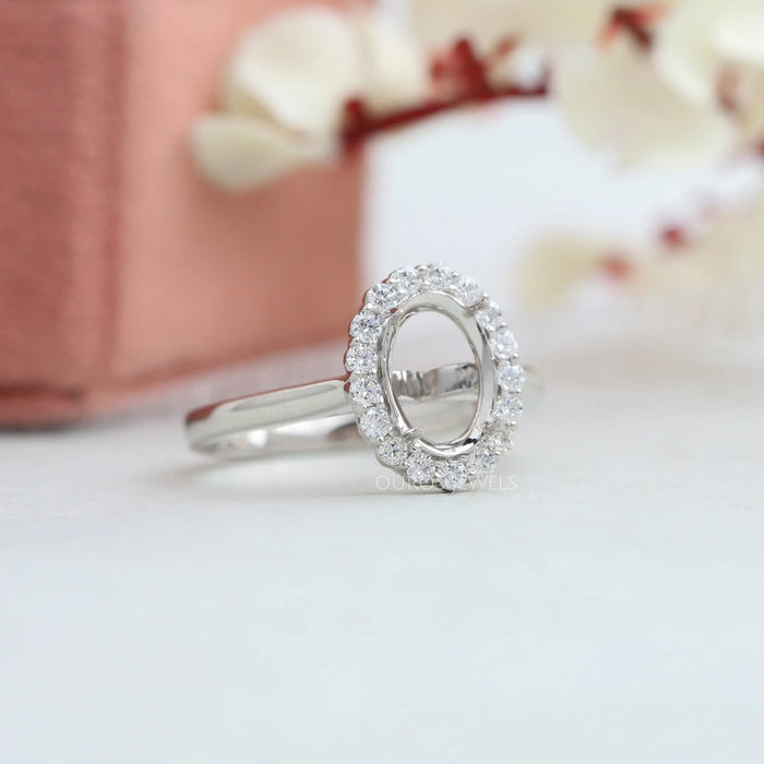 right side view of oval-shaped halo semi-mount engagement ring on grey fabric